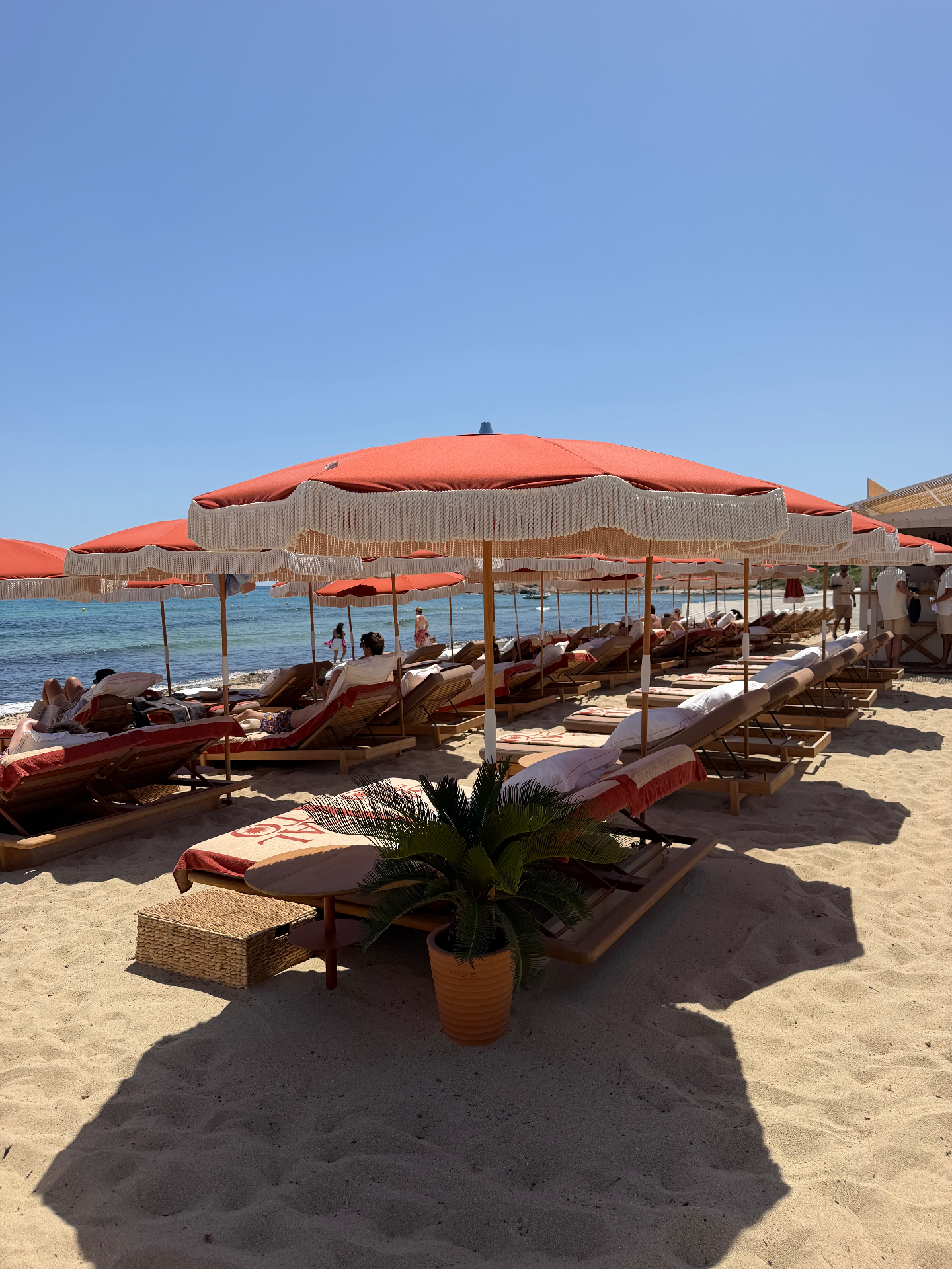 Rows of terracotta fringed parasols and wooden sun loungers on the sand at Pampelonne beach near Saint-Tropez, looking out to the turquoise Mediterranean.