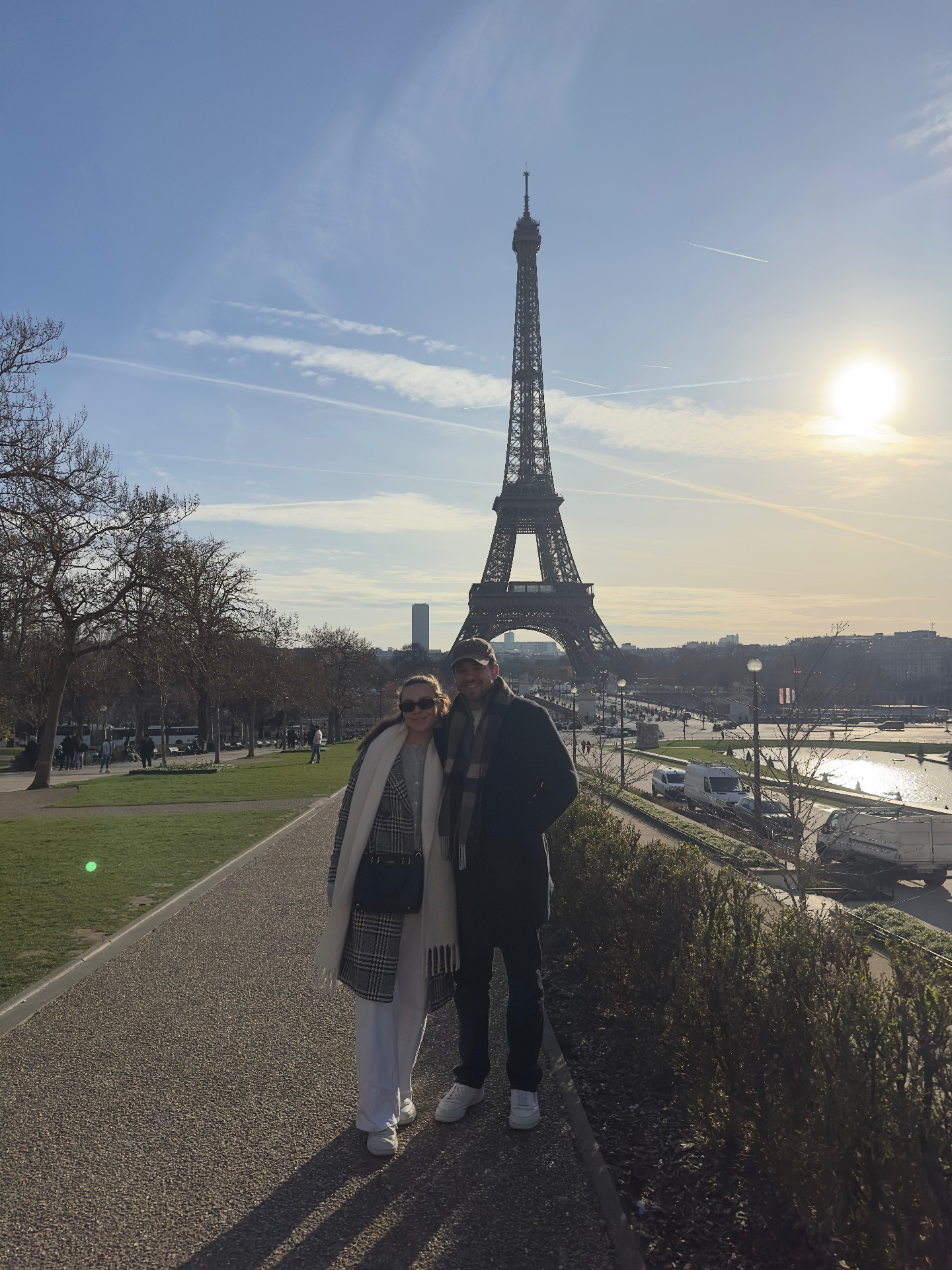 A couple standing on the Trocadéro promenade in winter with the Eiffel Tower and low golden sun behind them.